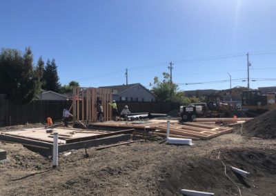 An image of general contractors framing a tiny home at Veteran's Village, Santa Rosa. A group of workers stabalize a wall segment as it is lifted into place