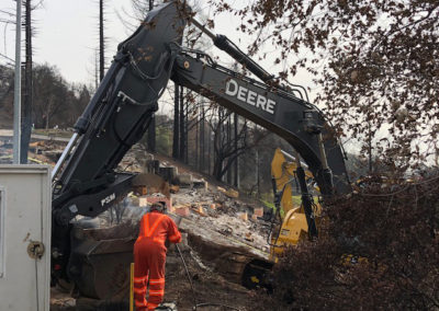 Contractors operating excavator during fires cleanup efforts.